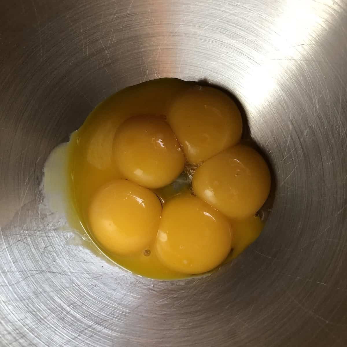 Five egg yolks in a KitchenAid stand mixer bowl ready to be whipped to pale yellow ribbons for tiramisu.