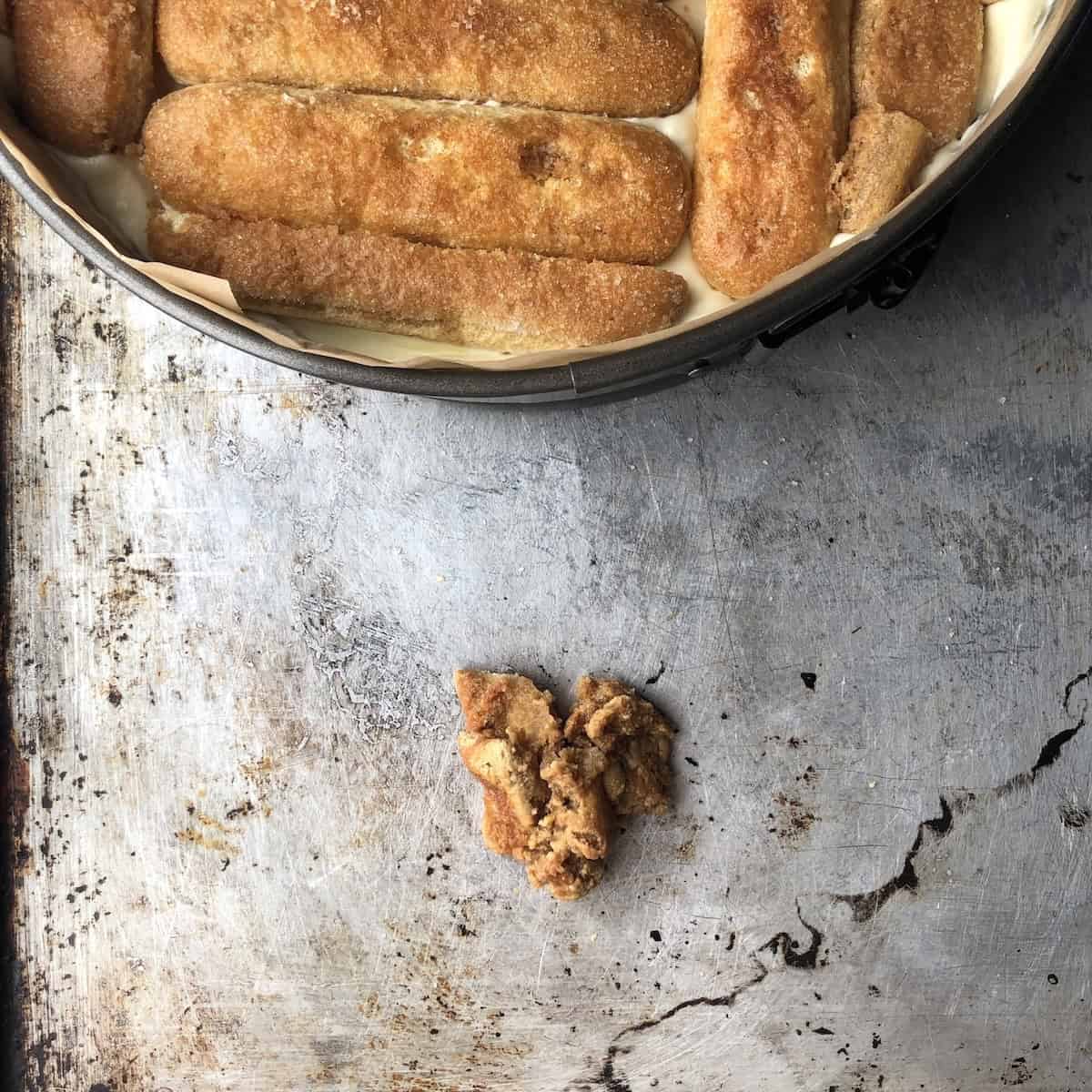 Pile of oversoaked soggy ladyfingers on a baking tray in front of tiramisu being layered, common mistake to avoid.
