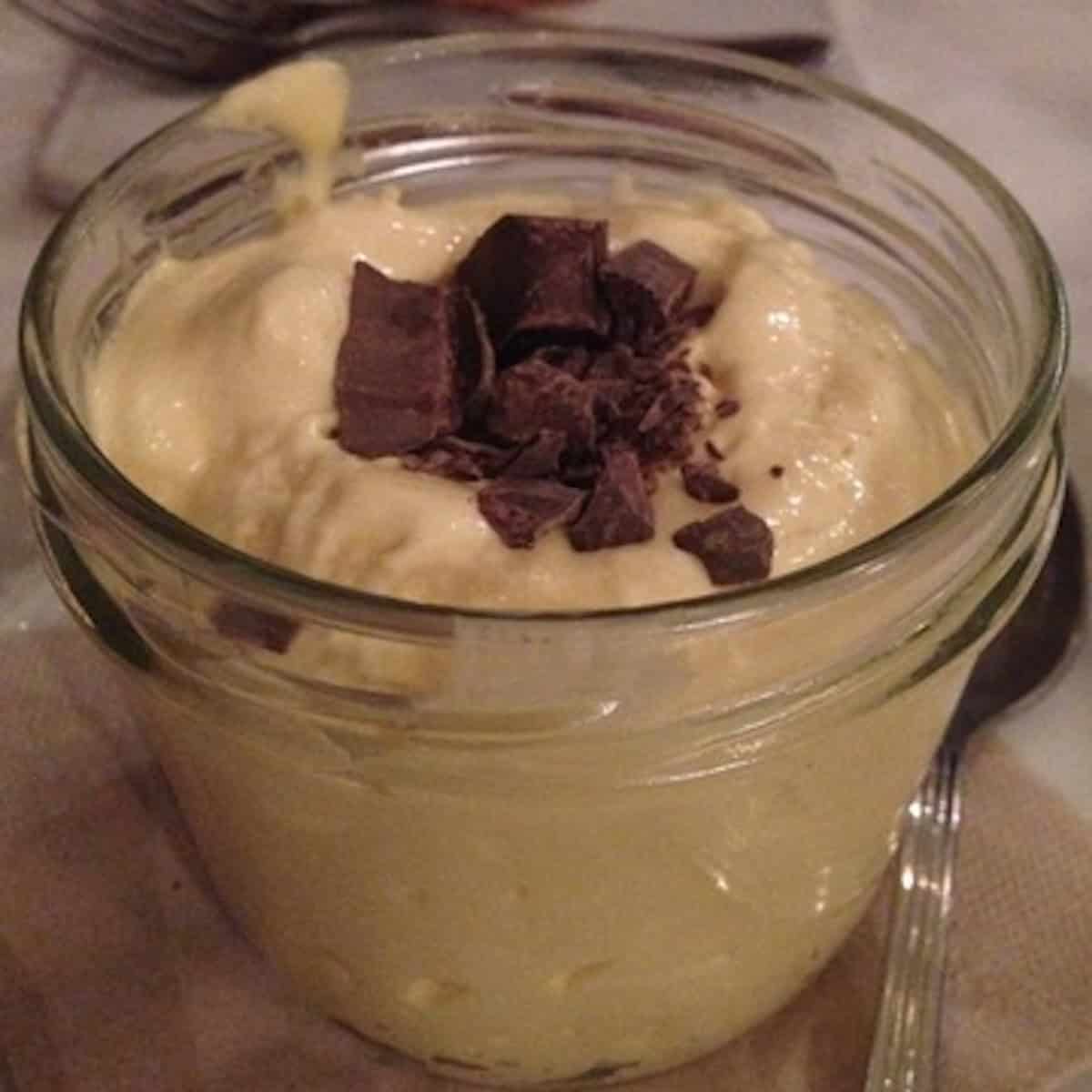 Italian restaurant tiramisu in a small canning jar with screw top lid, very creamy fluffy mascarpone with chopped chocolate on top and no cocoa powder and few ladyfingers.
