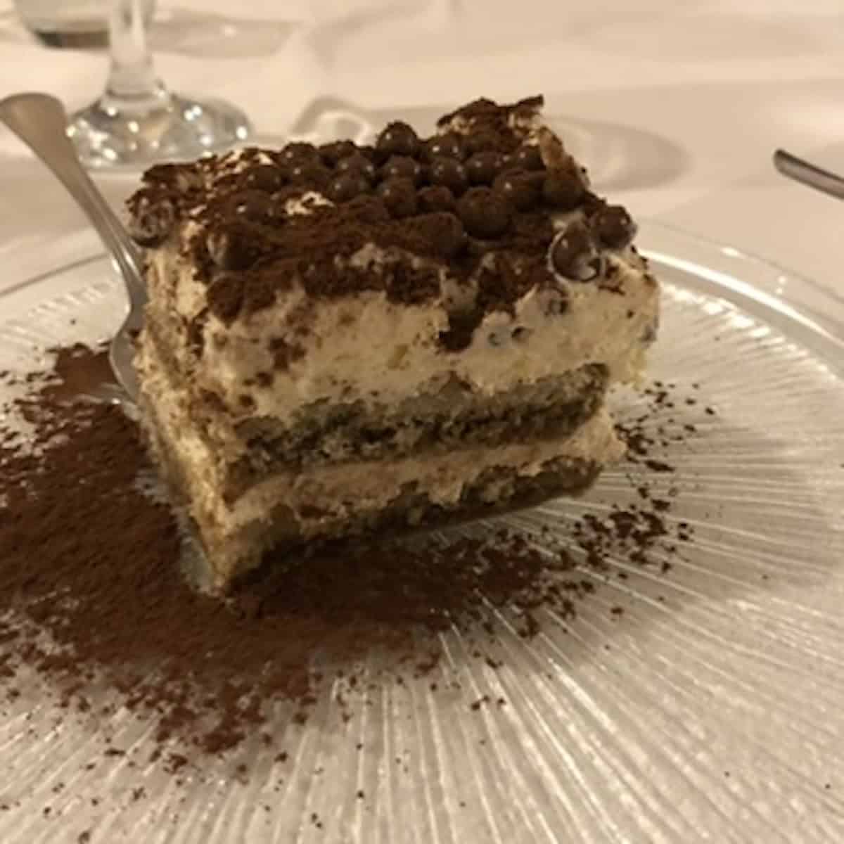 Two-layer square of restaurant tiramisu from a local Italian trattoria with Callebaut chocolate crisp balls and cocoa powder garnish, traditional tiramisu dessert.
