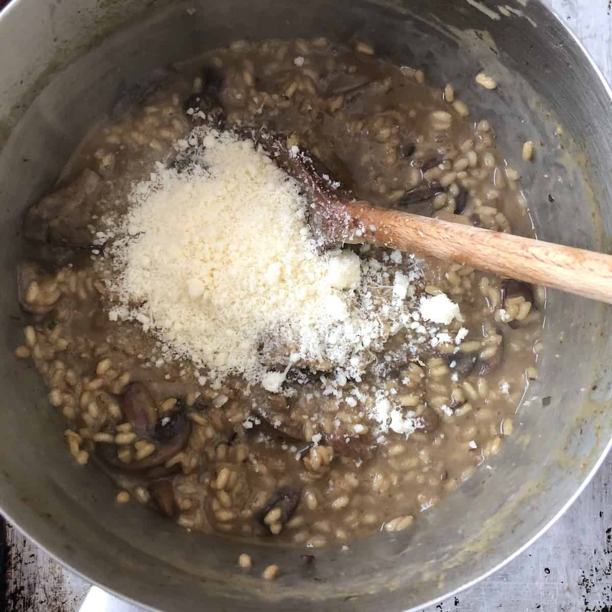 Grana padano cheese added to the mushroom risotto off the heat, parmesan risotto recipe finishing step for a velvety Italian risotto.
