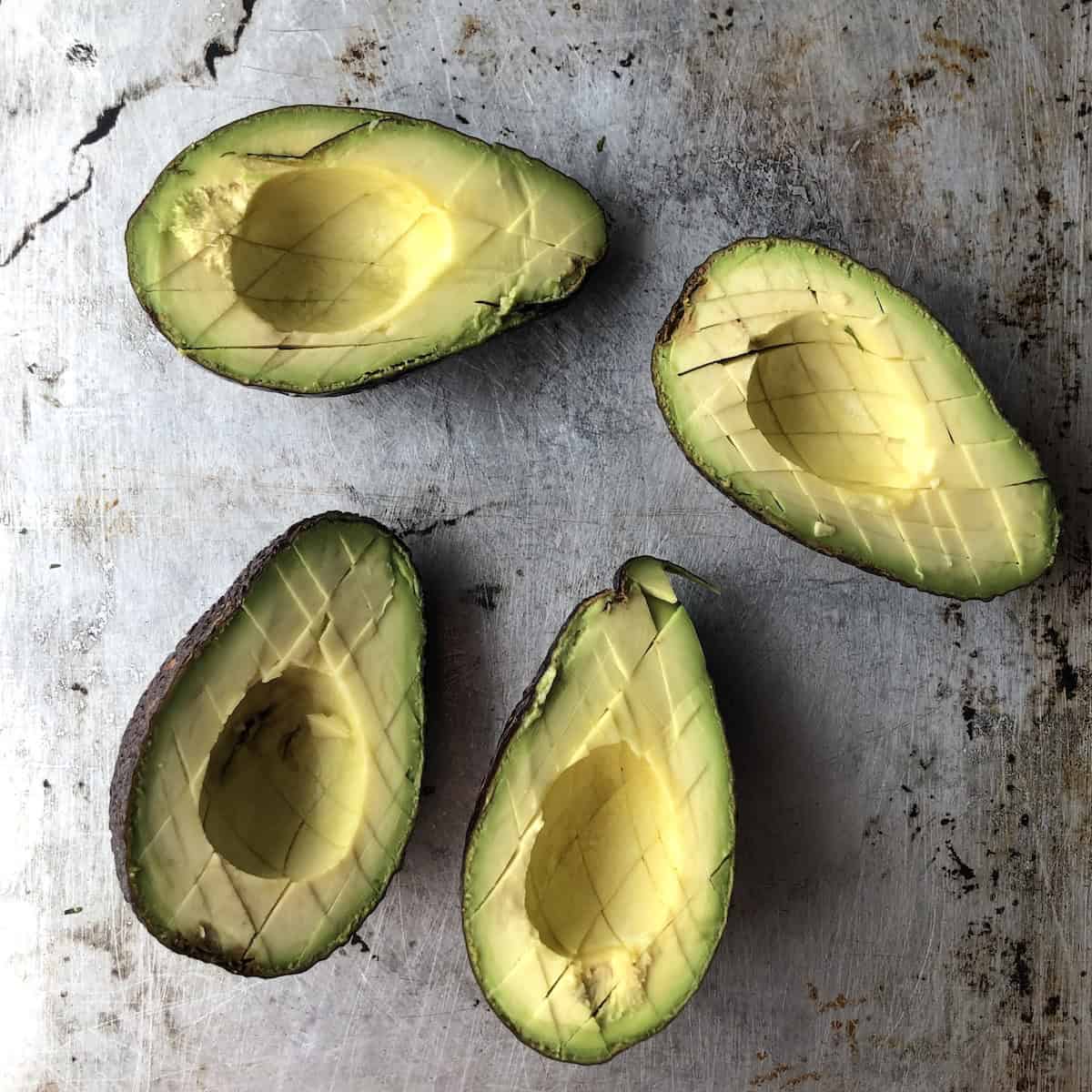 Four scored avocado halves ready to be added to the macerated aromatics for guacamole.
