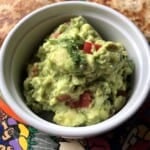 Creamy guacamole in a white ceramic ramekin with golden brown quesadillas on a plate.