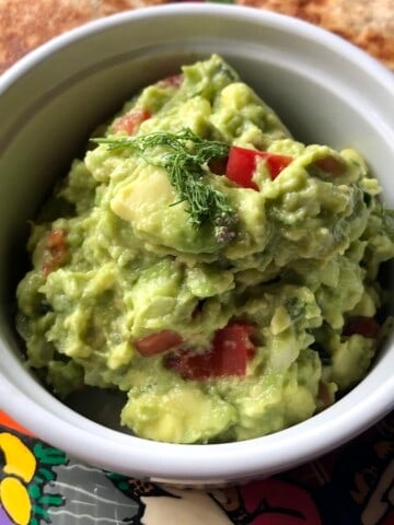 Creamy guacamole in a white ceramic ramekin with golden brown quesadillas on a plate.