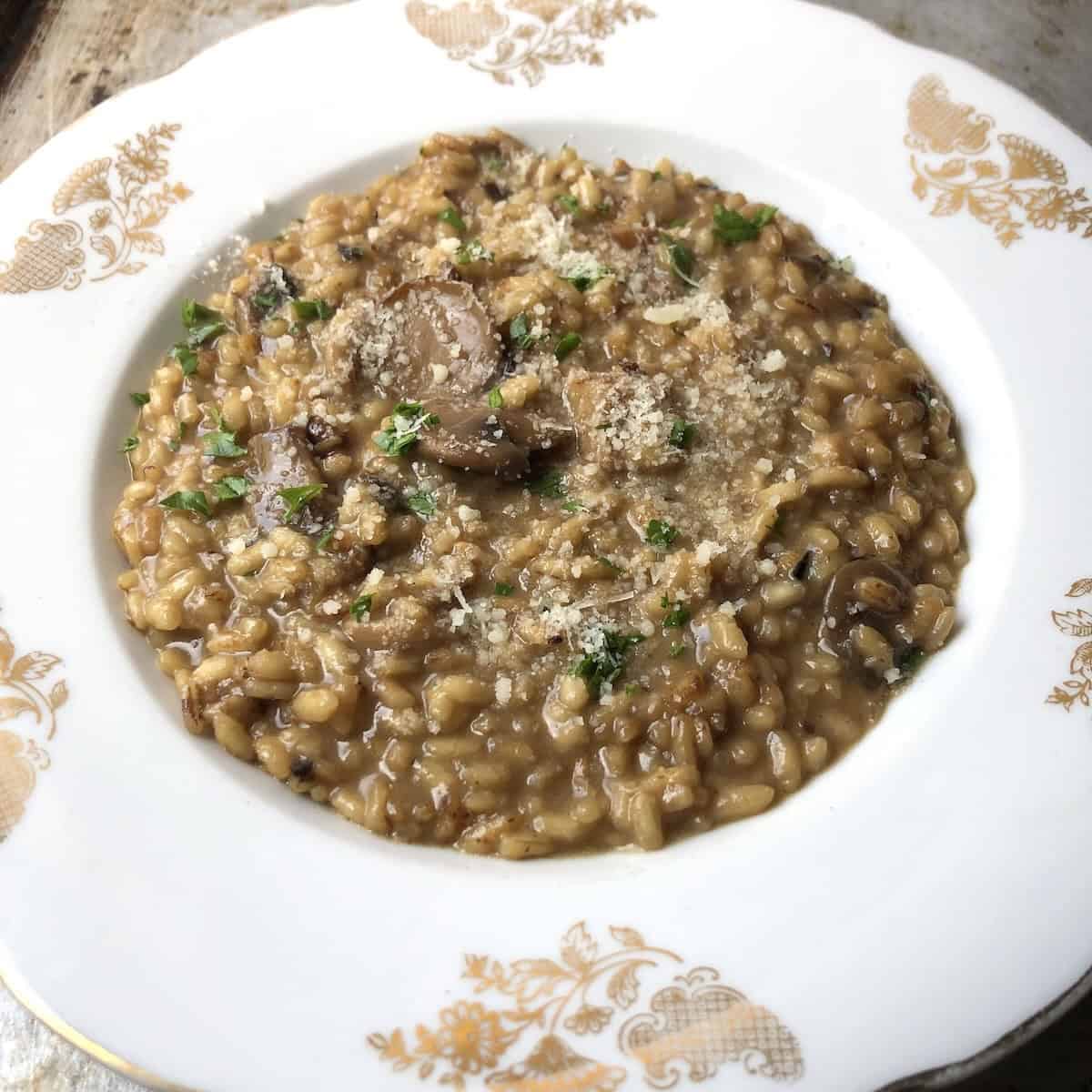 A bowl of creamy mushroom risotto garnished with minced parsley made with sauteed porcini and wild mushrooms (pioppini, oyster, and champignon) for an easy mushroom risotto you can make at home.