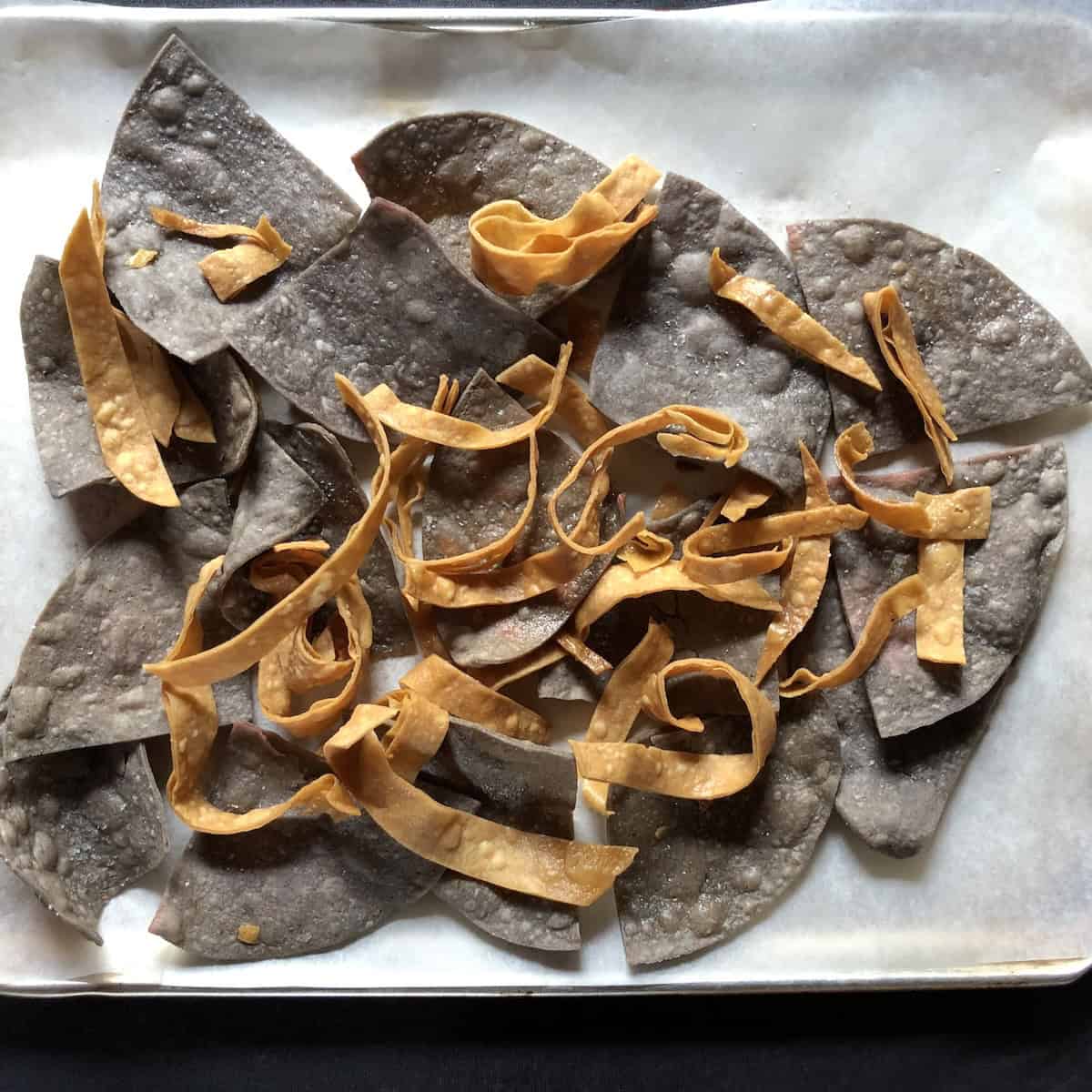 Freshly fried homemade blue corn and yellow corn tortilla chips on a paper towel lined tray for guacamole.
