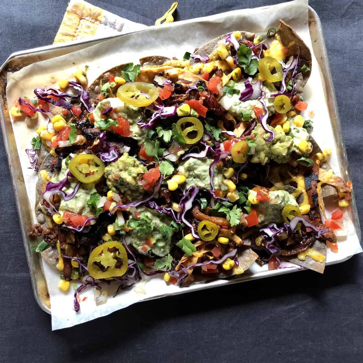 Sheet pan pulled pork nachos with shredded purple cabbage, iceberg lettuce, tomatoes, guacamole, cheese, jalapenos and fresh fried tortilla chips.
