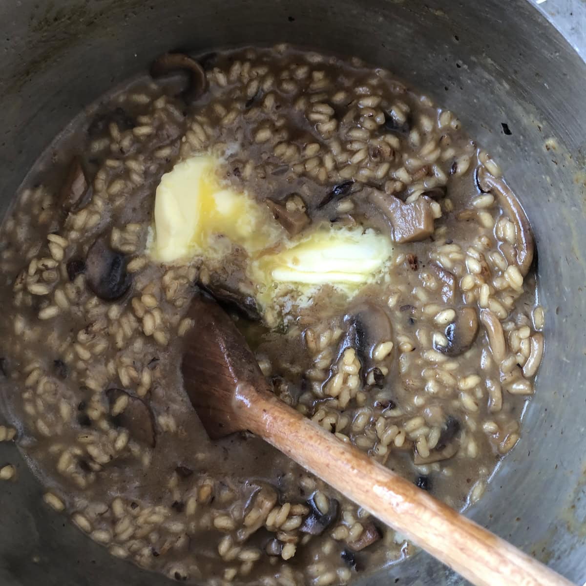 Butter added to the mushroom risotto off the heat for a rich and creamy risotto recipe, parmesan risotto technique of stirring in cold butter for silky texture.
