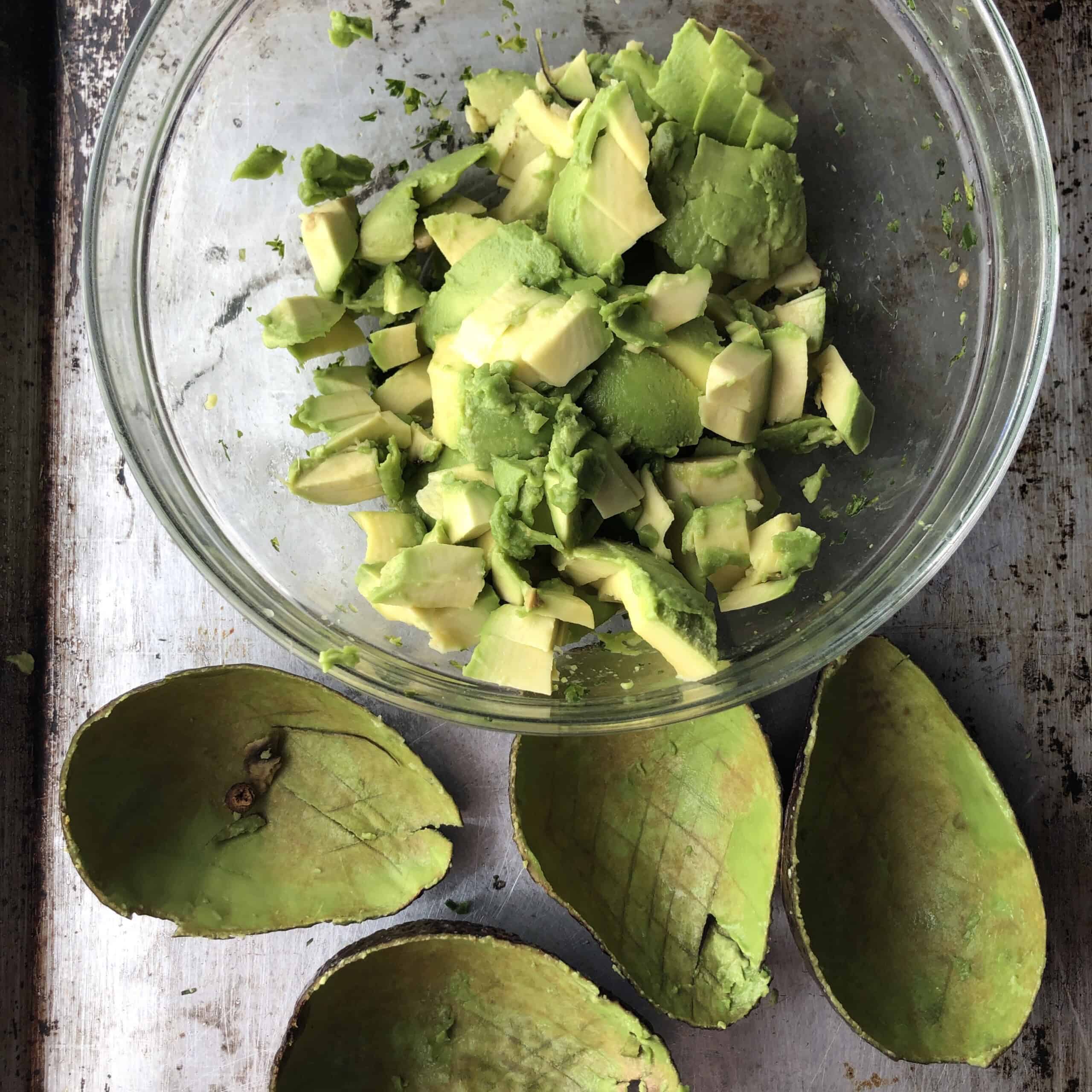 Scooped avocado flesh added to the bowl with macerated aromatics ready to mash for easy guacamole.
