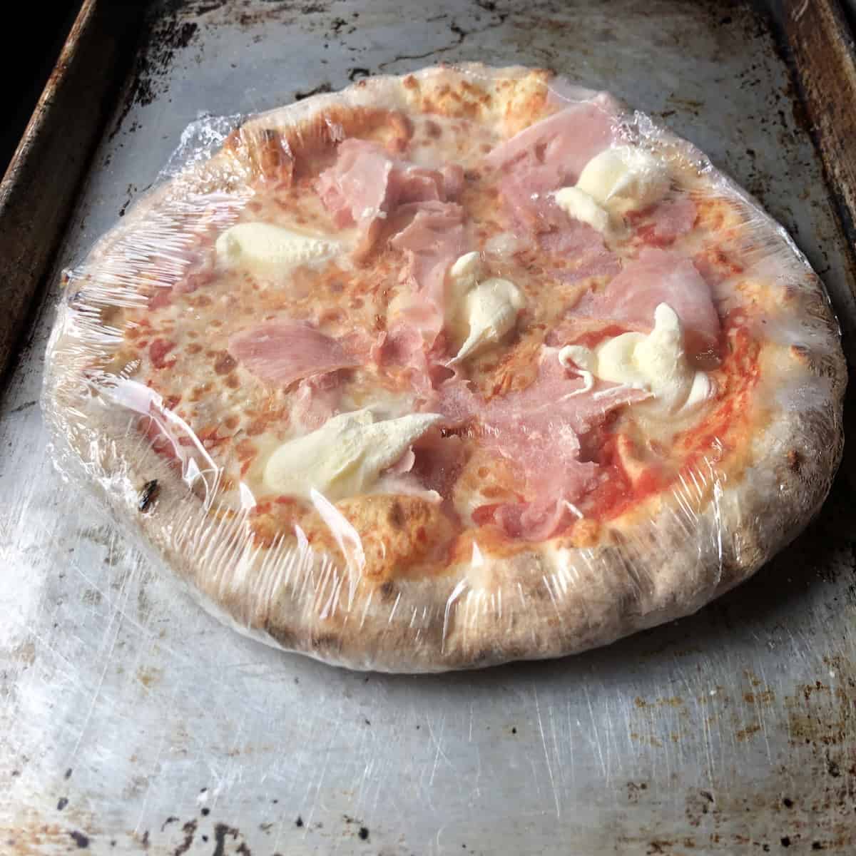 Frozen Italian handmade prosciutto praga and mascarpone pizza still in plastic before baking, commercial pizza dough recipe comparison for a homemade pizza crust version.