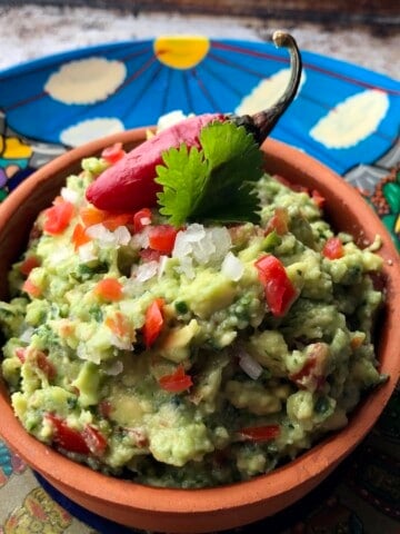 Easy guacamole recipe in a clay serving dish set on a colorful Mexican plate, simple homemade guacamole.