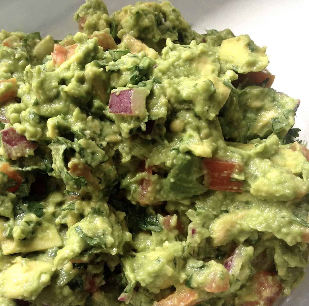 Bowl of homemade guacamole made with red onion as a variation also showing larger pieces of onion and tomatoes.
