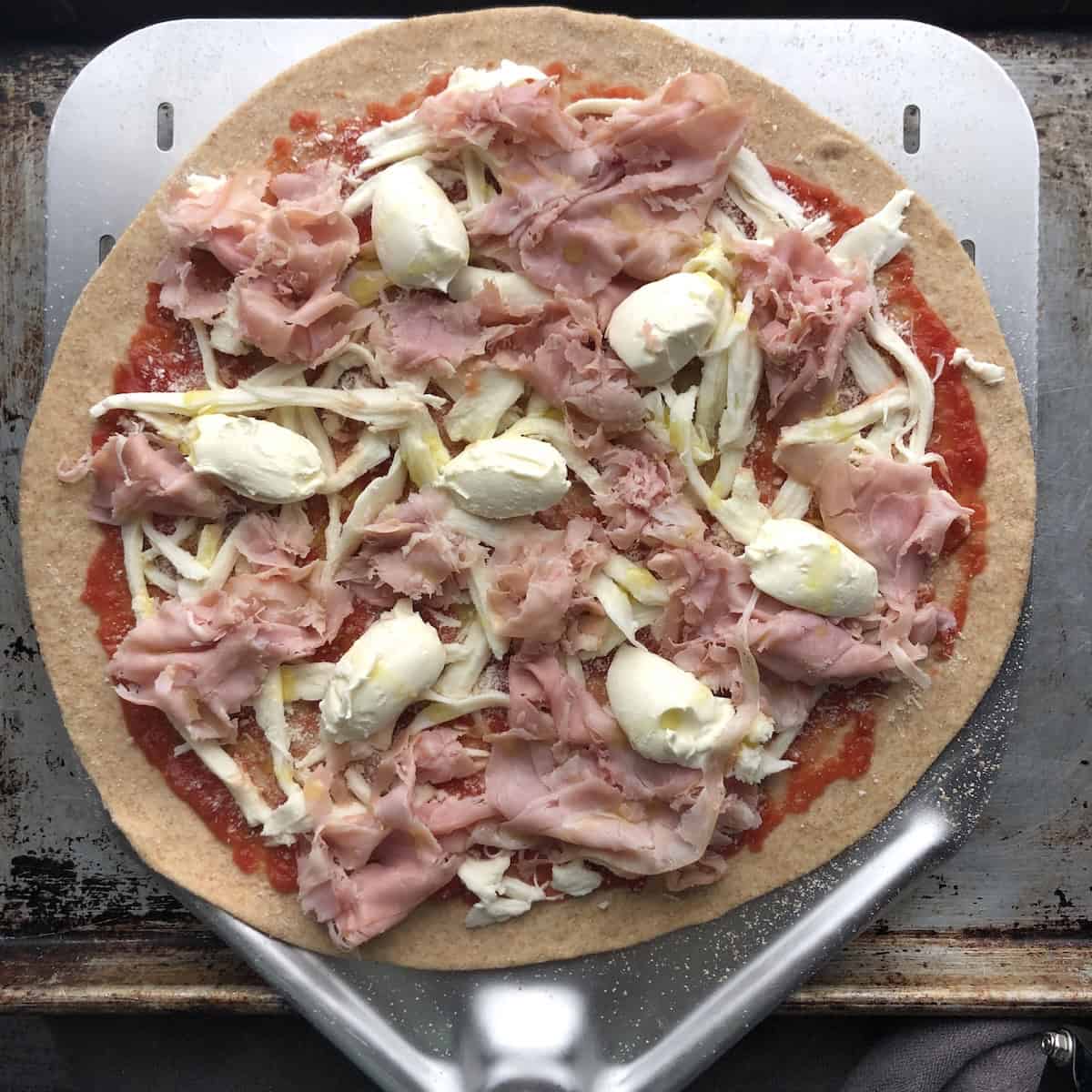Unbaked homemade prosciutto and mascarpone pizza topped and ready for the oven on a half whole wheat half bread flour pizza dough, easy homemade pizza recipe with a handmade pizza crust.