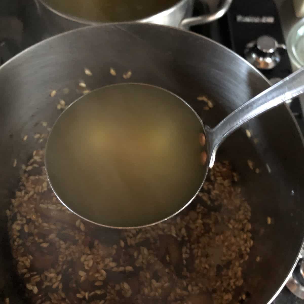 The first ladle of hot broth being added to the mushroom risotto, how do you make risotto by slowly adding broth one ladle at a time for a creamy risotto texture.


