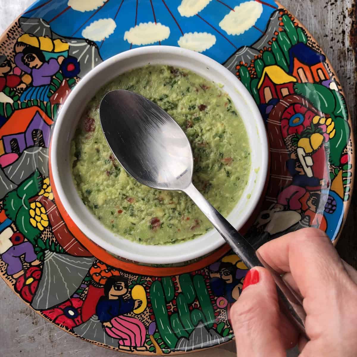 
Smoothing guacamole with a spoon in a ceramic freezer safe dish to remove air pockets before storing.
