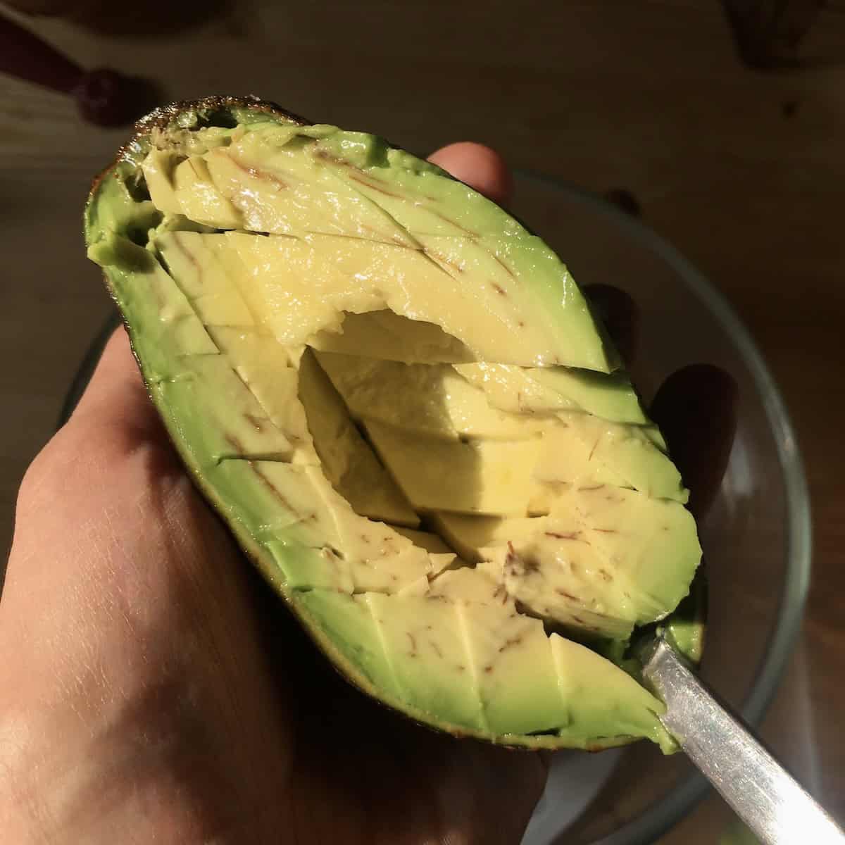 Scooping avocado flesh out of the skin using a spoon for guacamole.

