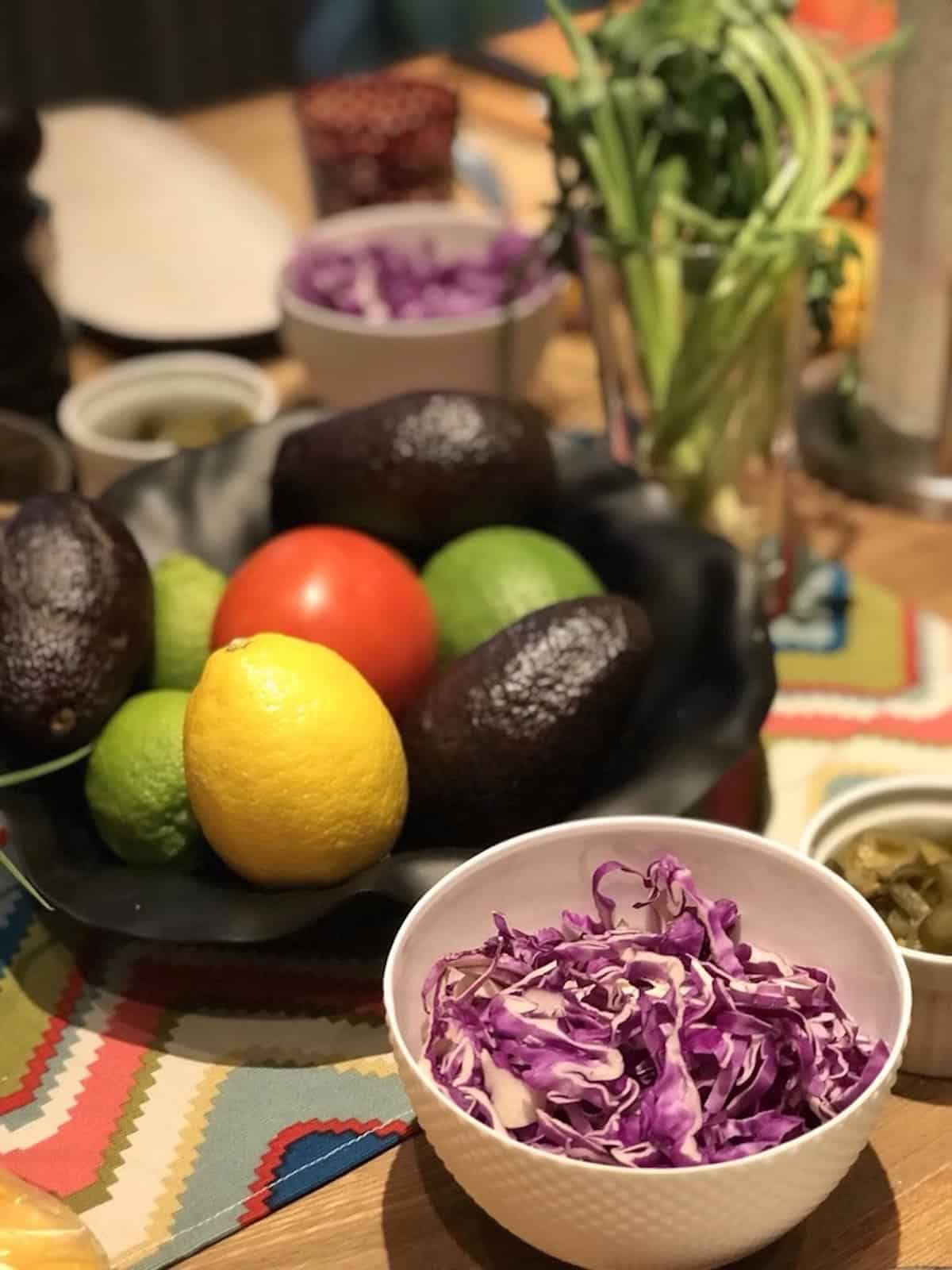 Whole Hass avocados in an Alessi fruit bowl with tomatoes, limes, shredded purple cabbage, and fresh cilantro for a guacamole and quesadilla cooking class in my Chengdu cooking school. 