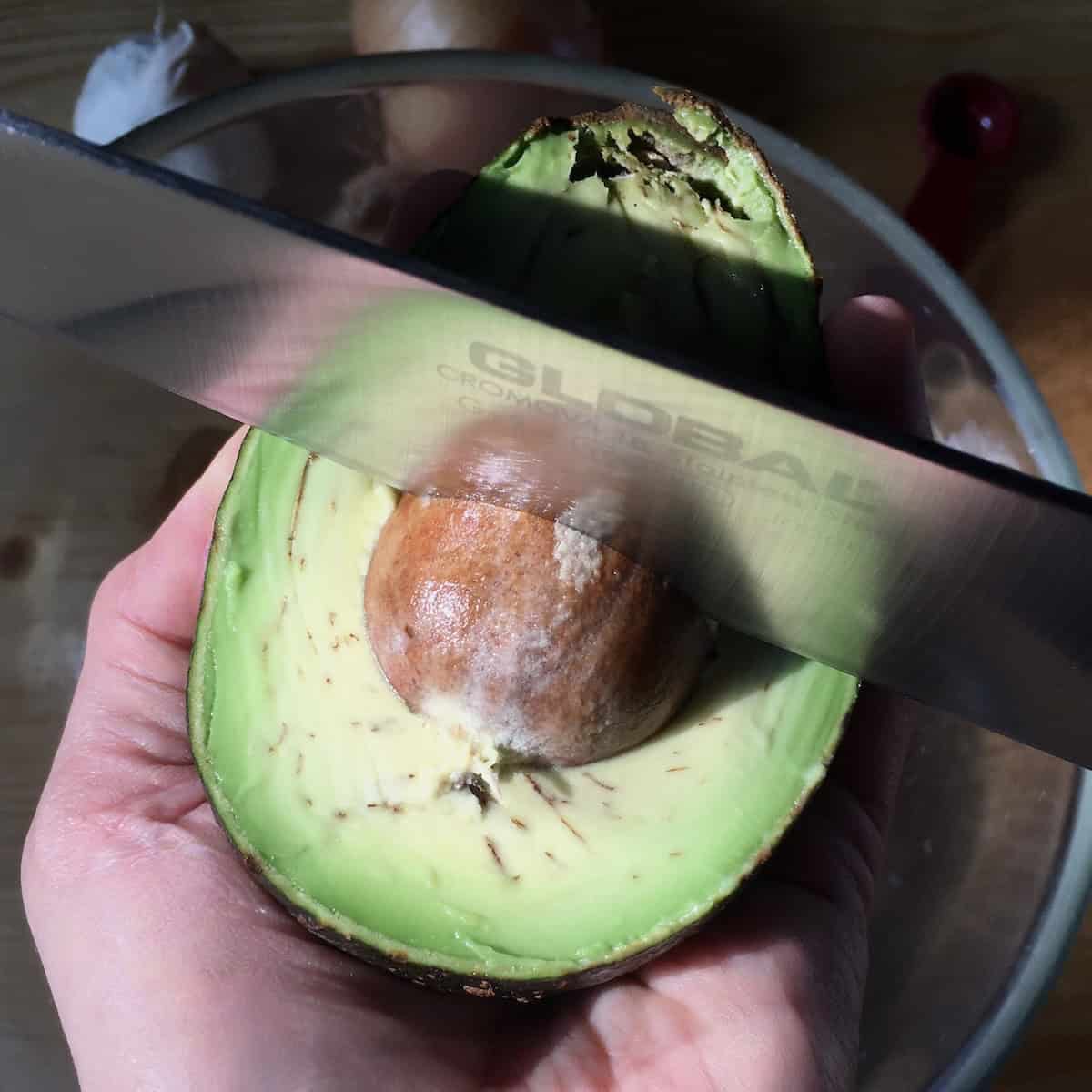 Popping the pit out of a Hass avocado using a Global chef's knife for guacamole.