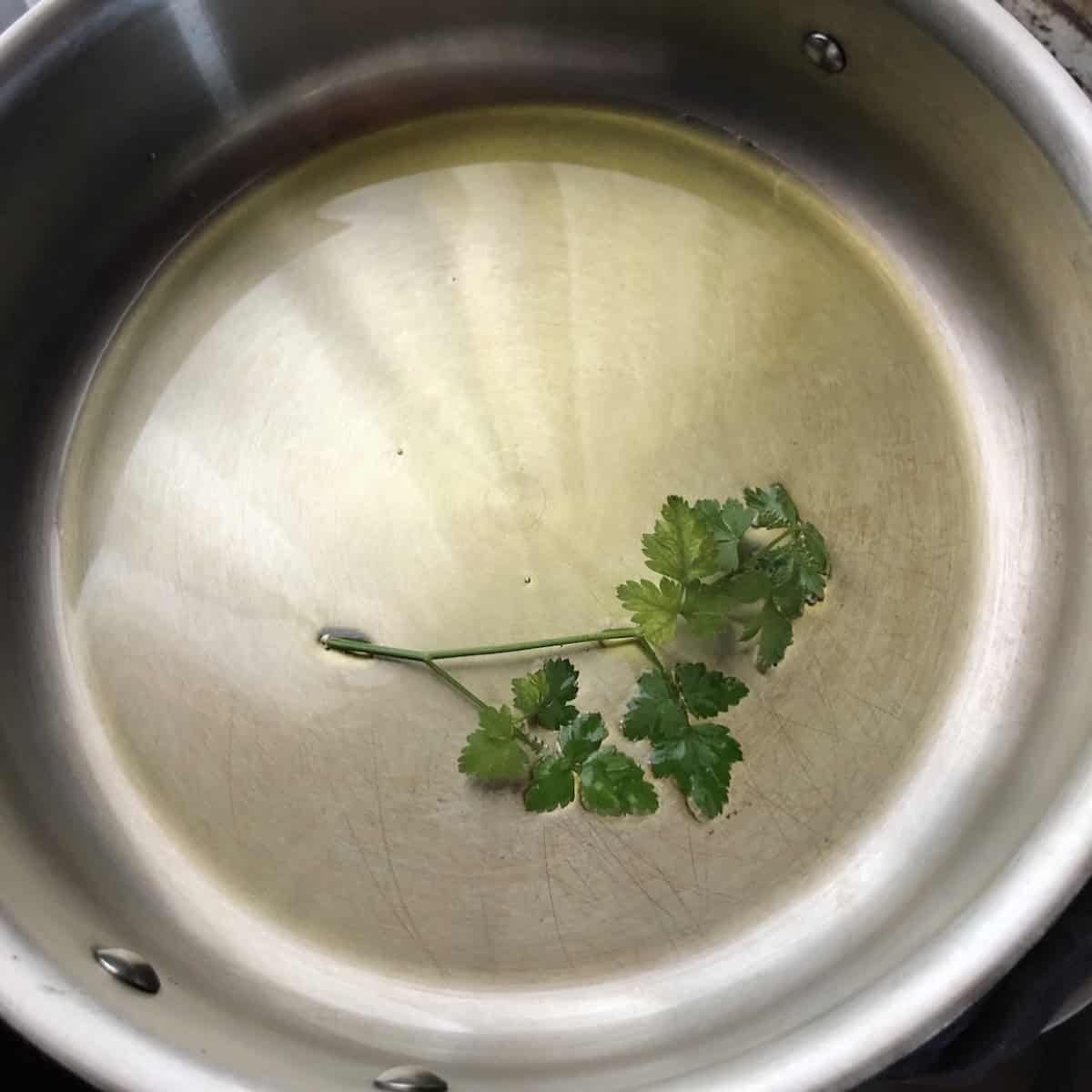 Olive oil heating in a saute pan with a sprig of fresh parsley, first step in how to make risotto for a homemade mushroom risotto recipe.
