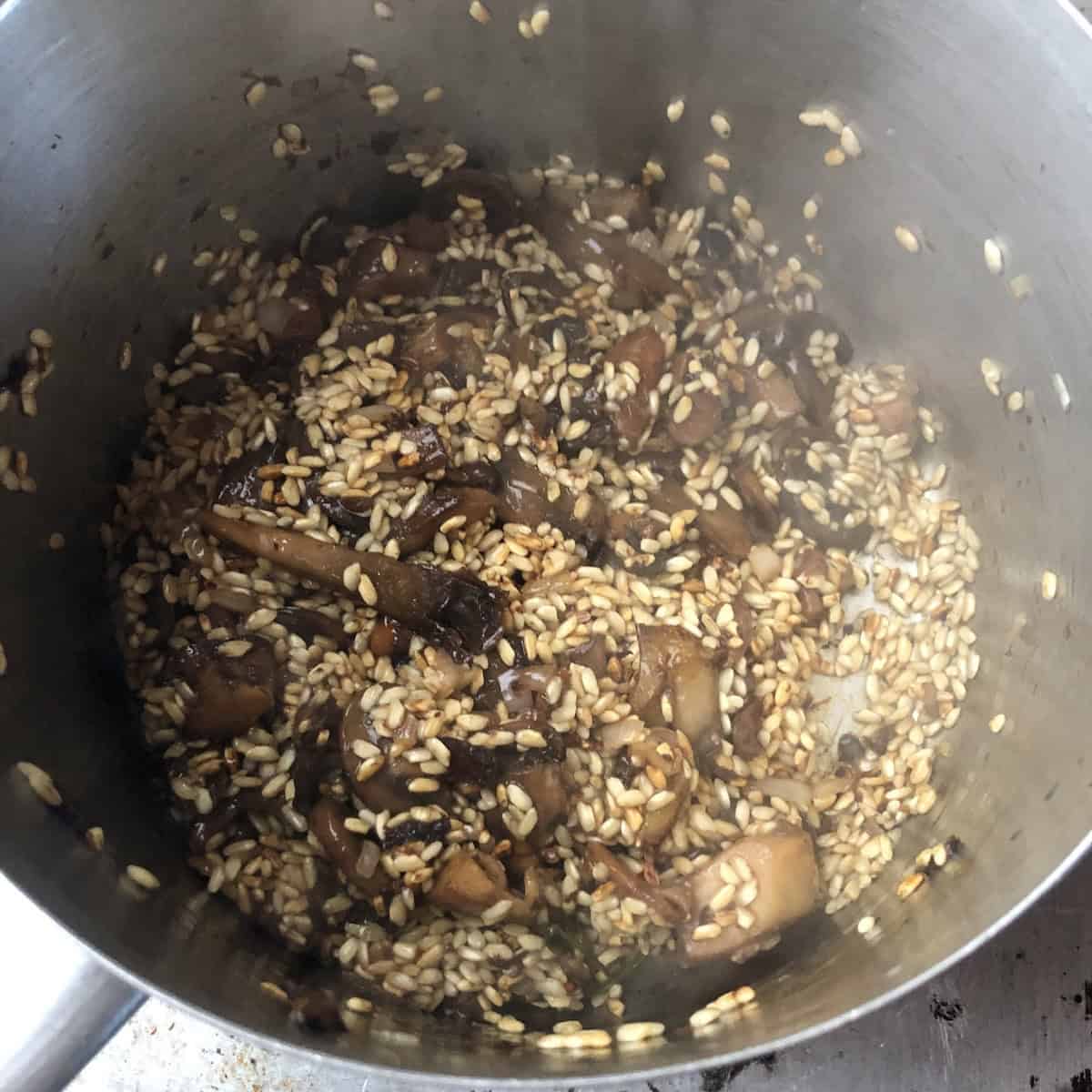 Mushroom risotto mixture stirred together in the pot before adding hot broth to begin cooking, easy mushroom risotto recipe ready for the slow addition of chicken stock.

