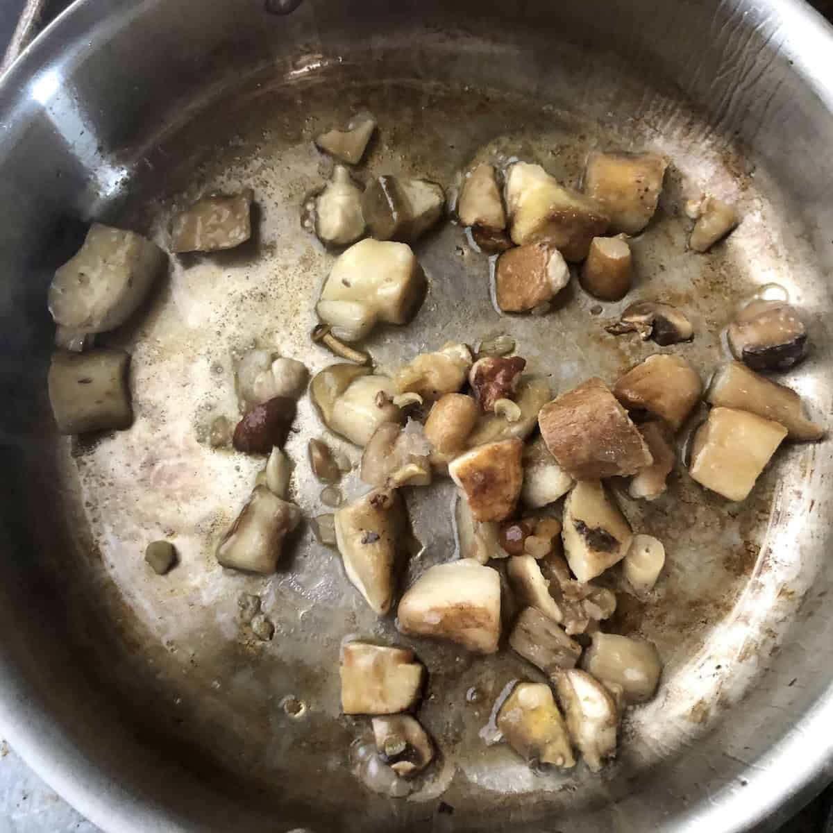 Frozen porcini mushrooms added to olive oil in a saute pan after removing the browned wild mushrooms, porcini risotto building layers of flavor for the best mushroom risotto.
