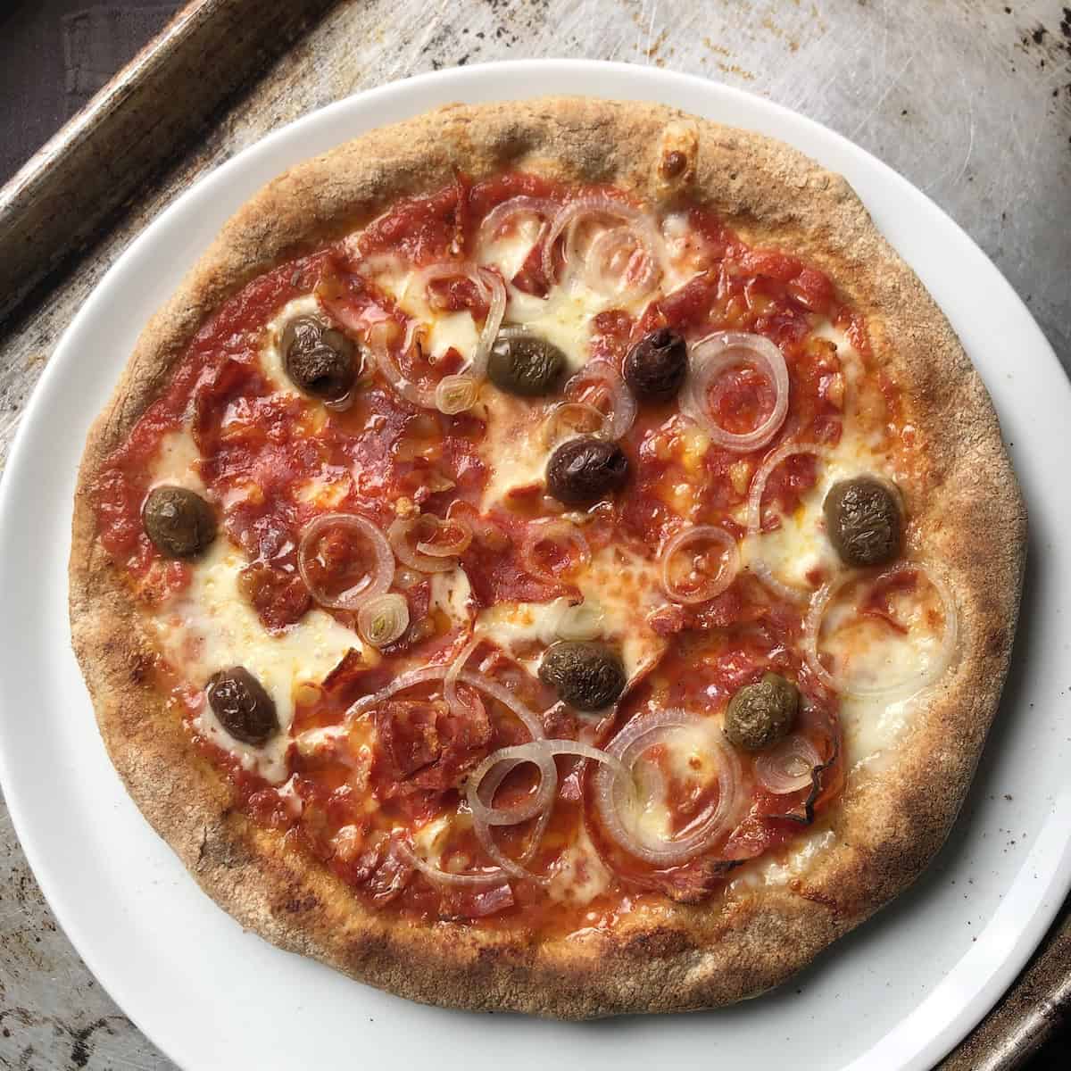 Baked pepperoni mushroom olive and onion pizza with buffalo mozzarella on a thick crust half whole wheat and half bread flour pizza dough.