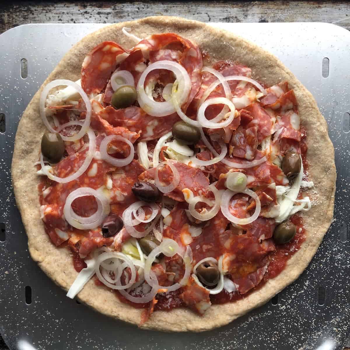 Unbaked pepperoni mushroom olive and onion pizza with buffalo mozzarella on a thick crust half whole wheat and half bread flour pizza dough.