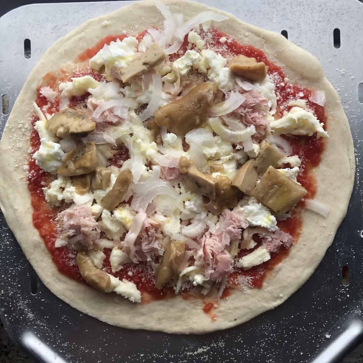 Unbaked porcini mushroom prosciutto cotto and onion pizza on a thin crust Caputo Nuvola 00 flour pizza dough ready for the oven.