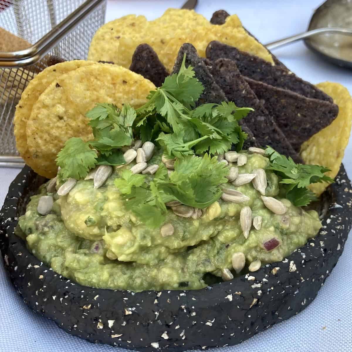 Watery looking guacamole served with toasted sunflower seeds at an Italian restaurant, not made with Hass avocados.
