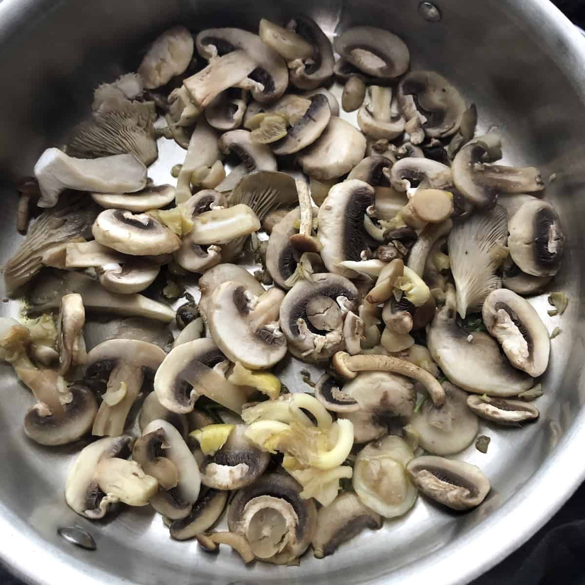 Adding fresh wild mushrooms to olive oil and parsley in a saute pan to brown for wild mushroom risotto, cooking risotto with fresh mushrooms first for the best flavor.
