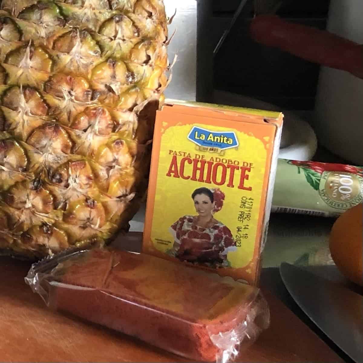 A box of achiote paste on a cutting board next to a fresh pineapple for making Mexican recipes like pollo asado, tacos al pastor, etc.