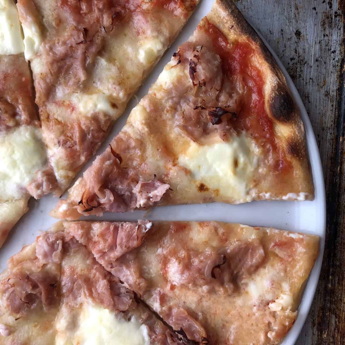 A fully baked prosciutto cotto and mascarpone pizza, sliced and ready to eat (one of our favorite pizza toppings ever!
