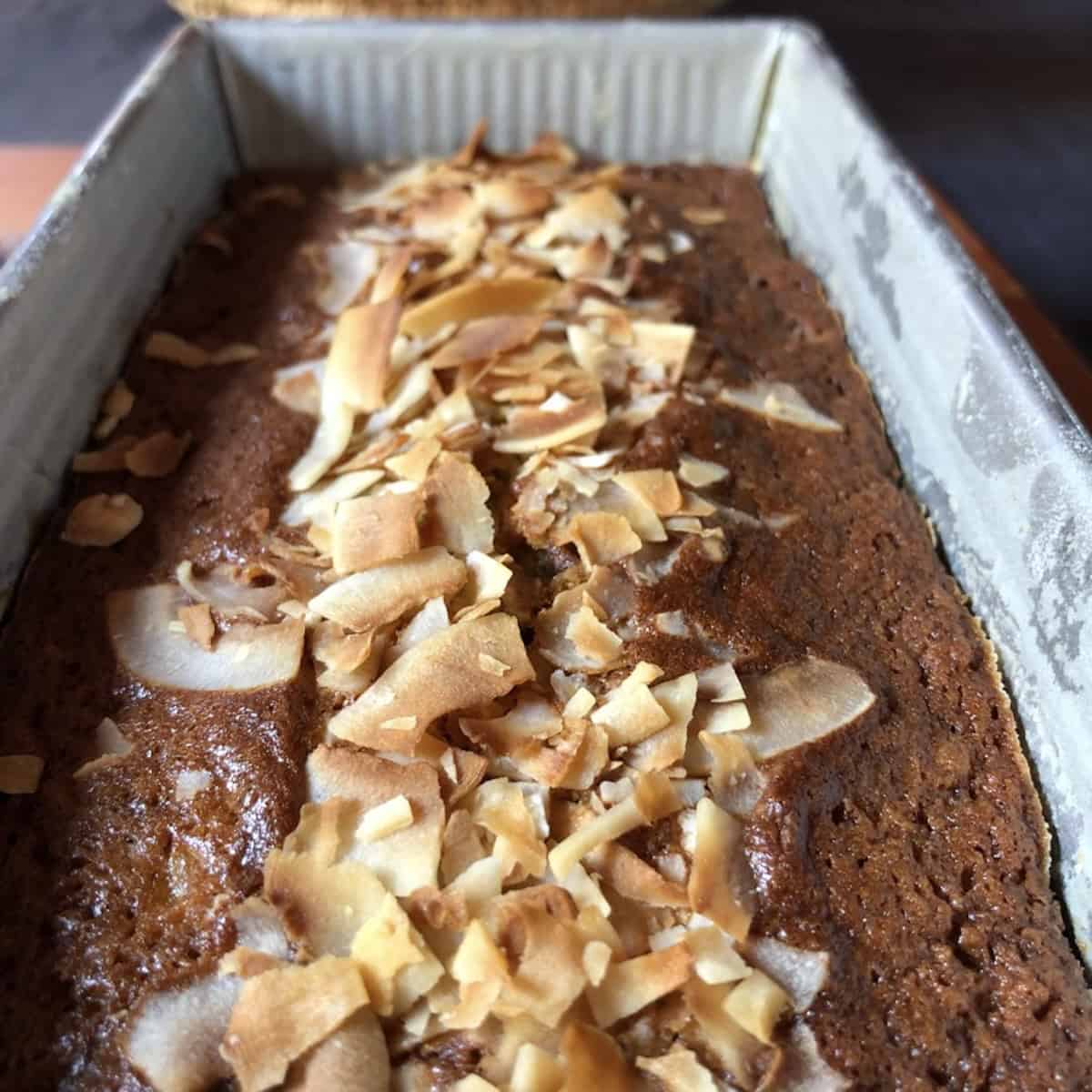 Closeup of a fully baked banana bread with chocolate chips and coconut in a loaf pan with golden brown toasted coconut flakes on top.