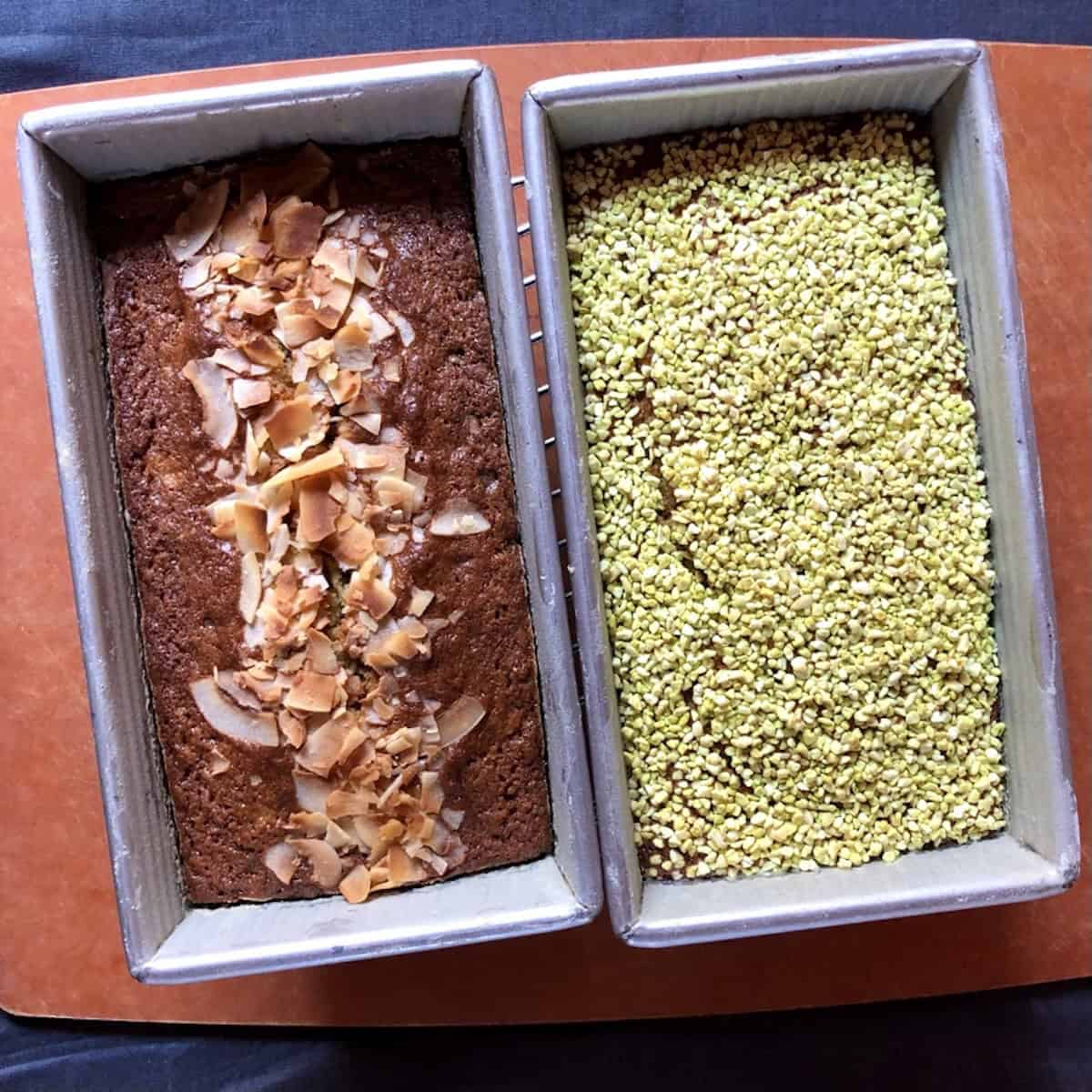 Two loaf pans of baked banana bread varieties with coconut chocolate chip banana bread on the left and pecan pistachio banana bread on the right.
