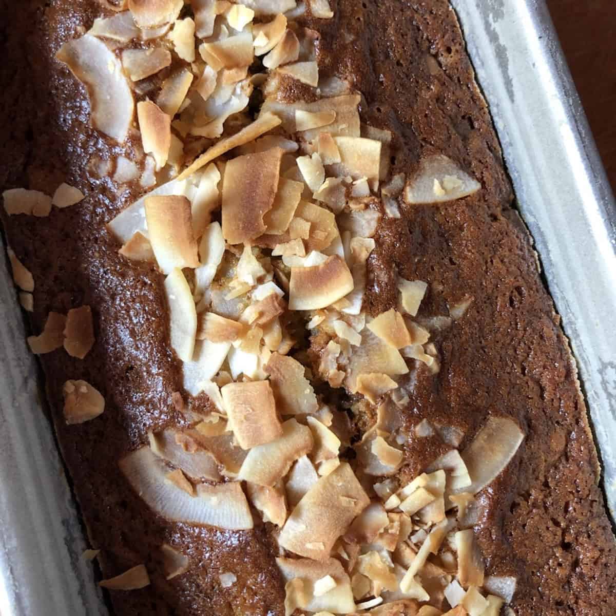 Closeup of a fully baked banana bread with chocolate chips and coconut in a loaf pan with golden brown toasted coconut flakes on top.