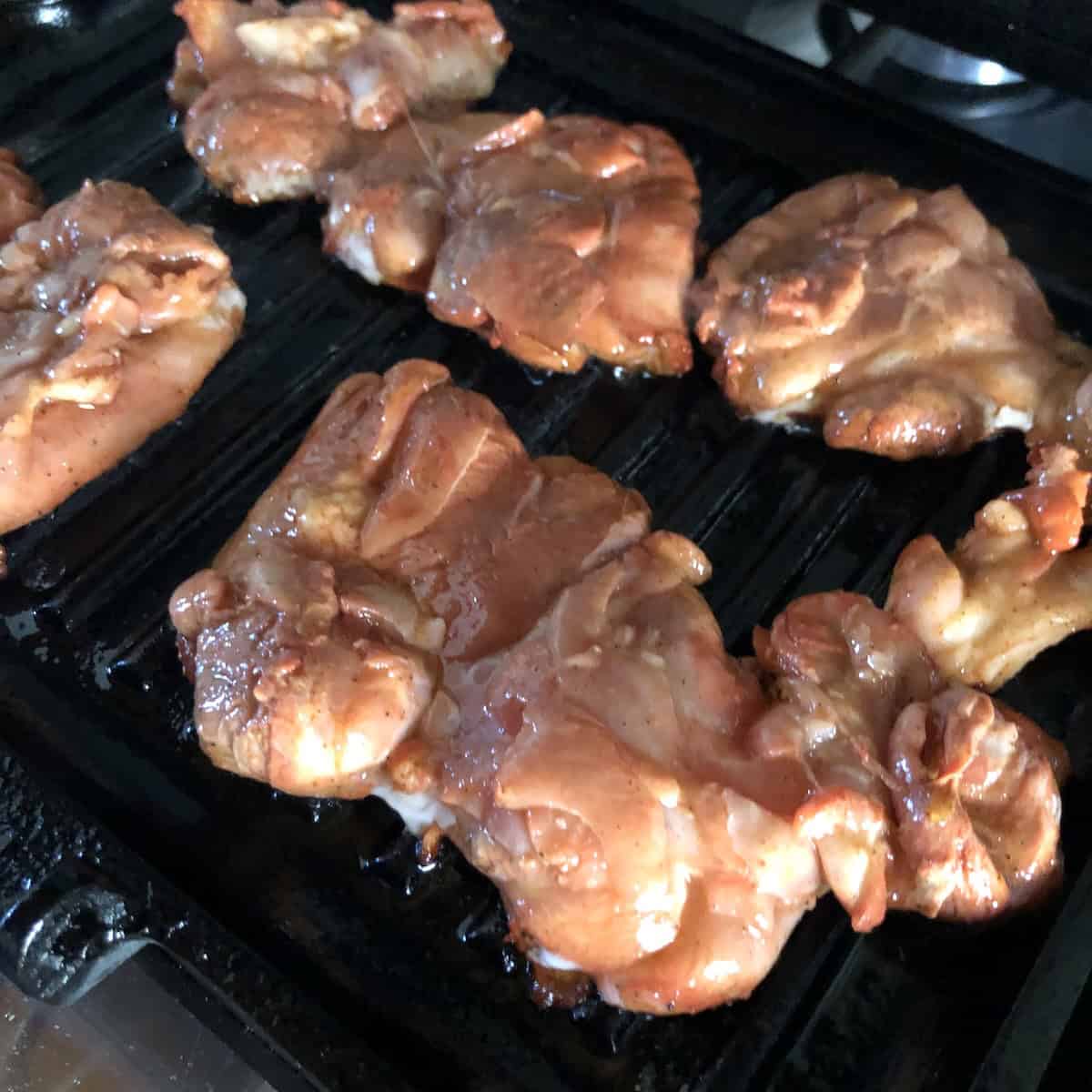 Pollo asado chicken cooking on a grill pan looking paler and opaque and slightly curling at the edges indicating it is time to flip, showing how to cook chicken asada on the stovetop.

