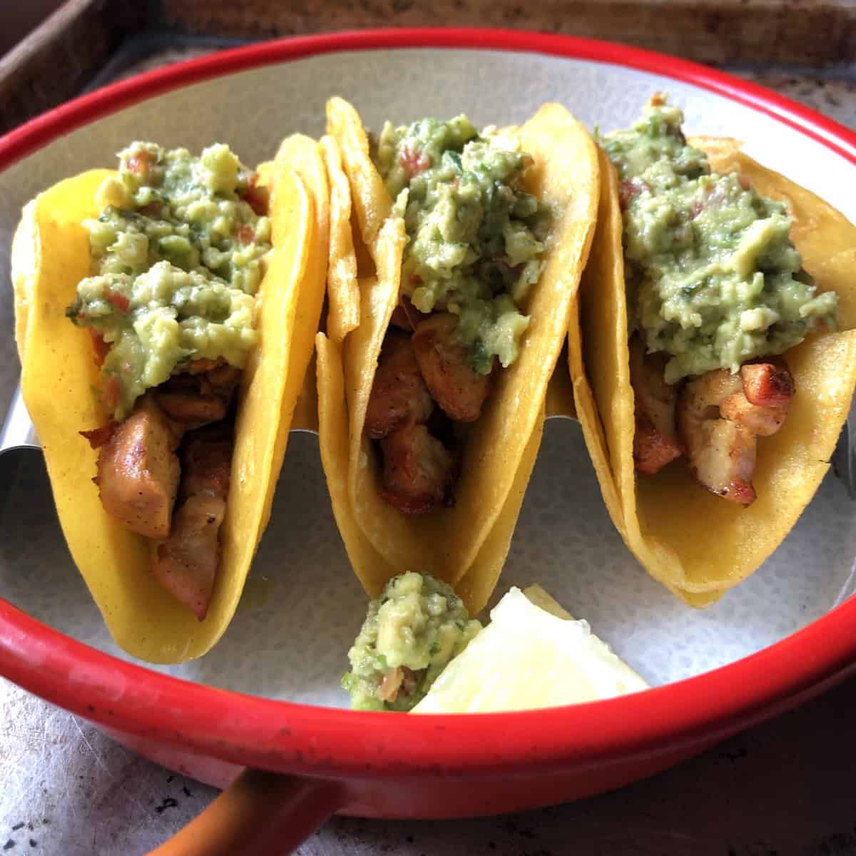 Three chicken tacos with sliced pollo asado and homemade guacamole in a stainless steel taco holder before adding the cabbage.
