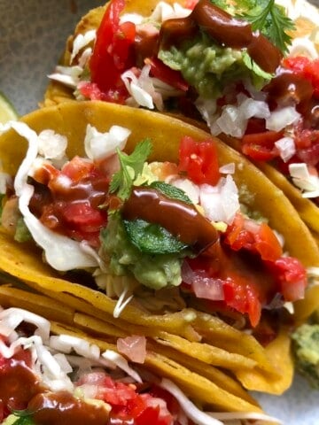 Fully loaded pollo asado chicken tacos with guacamole, salsa, shredded cabbage, diced onions, cilantro, jalapeno, and hot sauce with lime wedges, pollo asado tacos recipe.