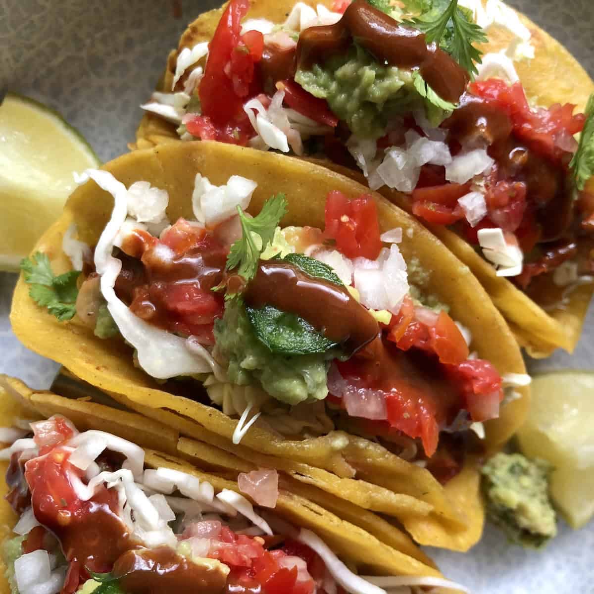 Fully loaded pollo asado chicken tacos with guacamole, salsa, shredded cabbage, diced onions, cilantro, jalapeno, and hot sauce with lime wedges, pollo asado tacos recipe.