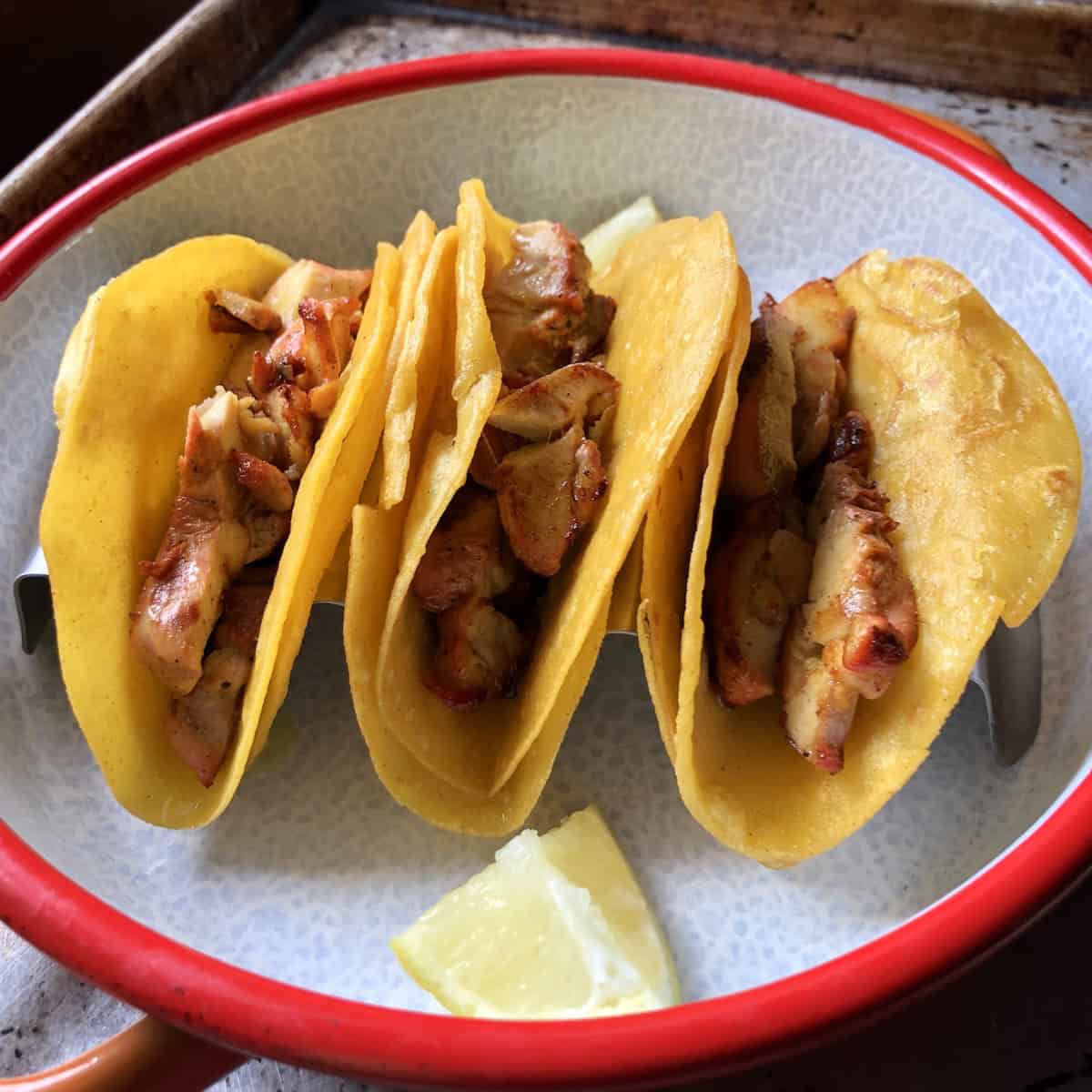 Two warmed corn tortillas with sliced pollo asado piled inside in a taco holder showing the first layer of pollo asado tacos.
