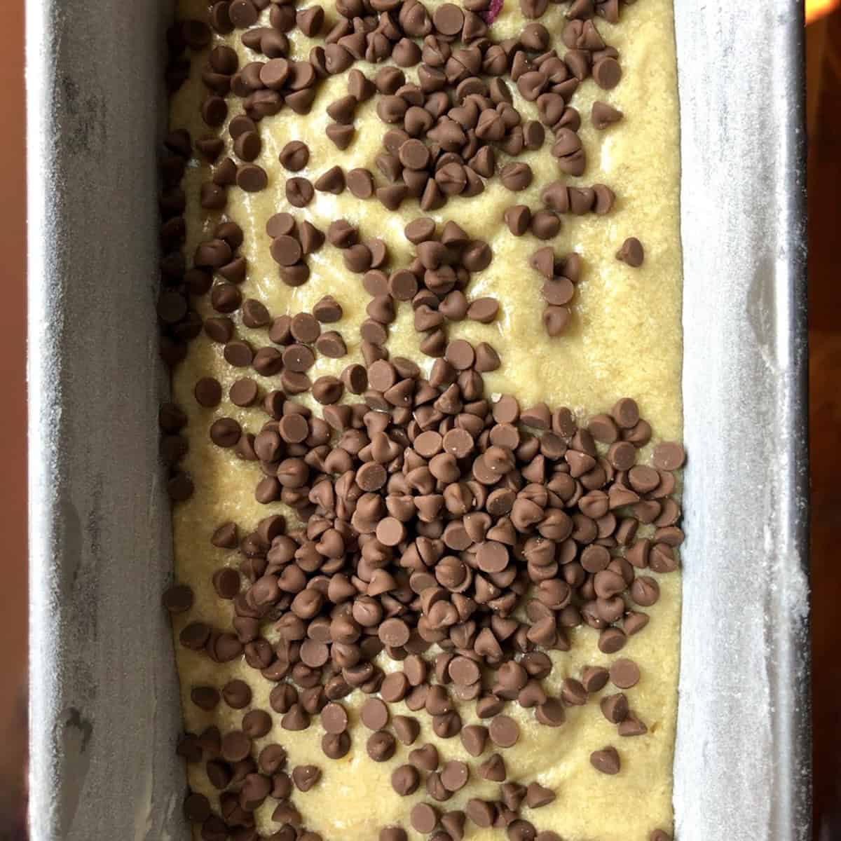 Chocolate chip coconut banana bread batter in a loaf pan with chocolate chips added and ready to be mixed in.
