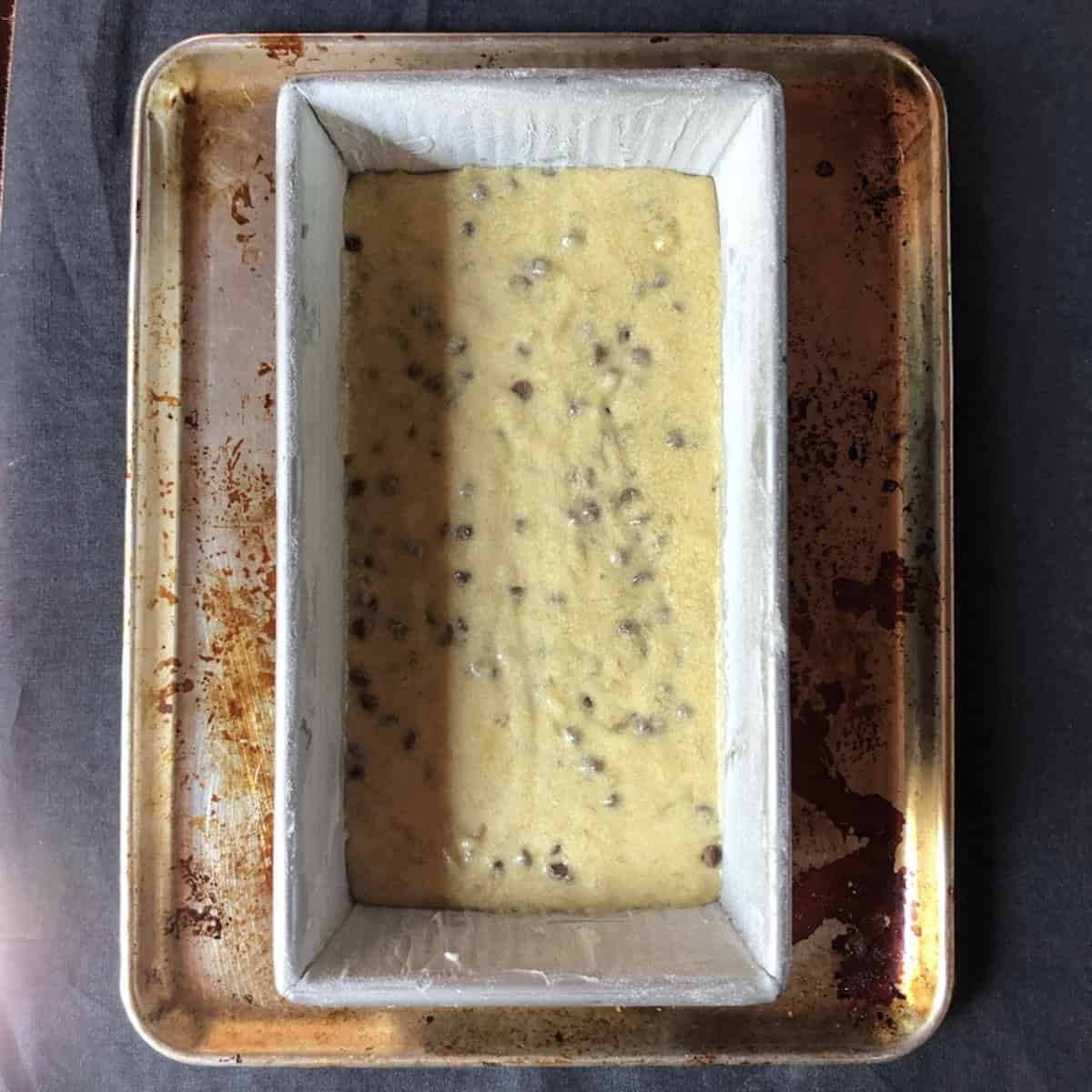 Chocolate chip coconut banana bread batter in a loaf pan with chocolate chips mixed in, coconut chocolate chip banana bread ready for the coconut topping.
