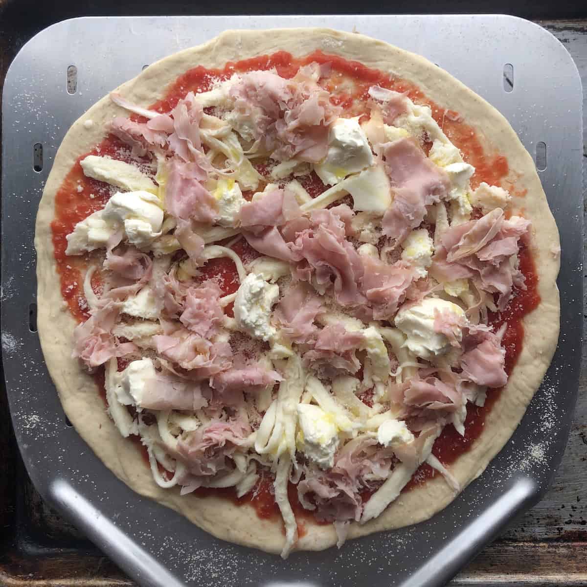 Unbaked homemade prosciutto and mascarpone pizza topped and ready for the oven on an 00-flour pizza dough, easy homemade pizza recipe with a handmade pizza crust.