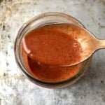 A spoon of pollo asado marinade held above the jar showing flecks of real Mexican spices and the ideal smooth consistency showing how to make a pollo asado marinade recipe from scratch.