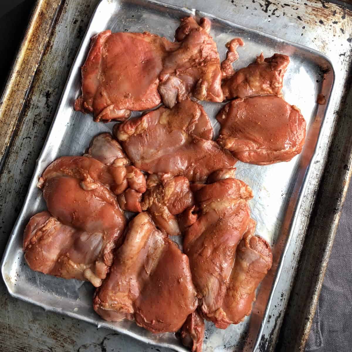 Thinner pollo asado marinated chicken thighs on a silver baking tray patted dry and brushed with oil ready to grill,  showing how to make mexican grilled chicken from scratch. 

