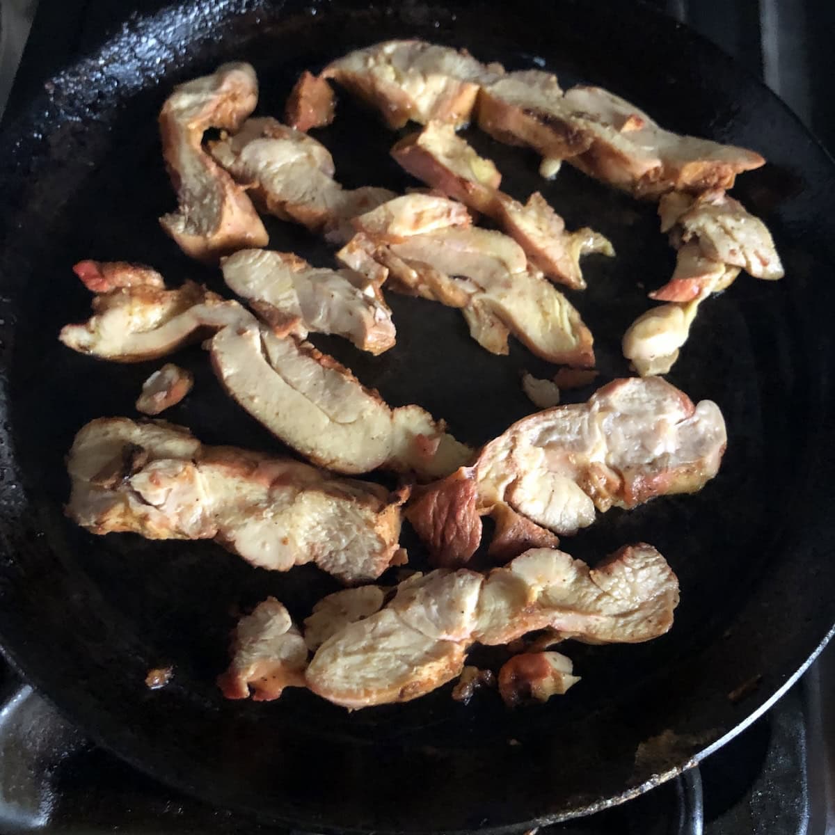 Previously frozen meal-prepped pollo asada slices thawed and added to a lightly oiled cast iron pan to reheat, pollito asado ready to serve.

