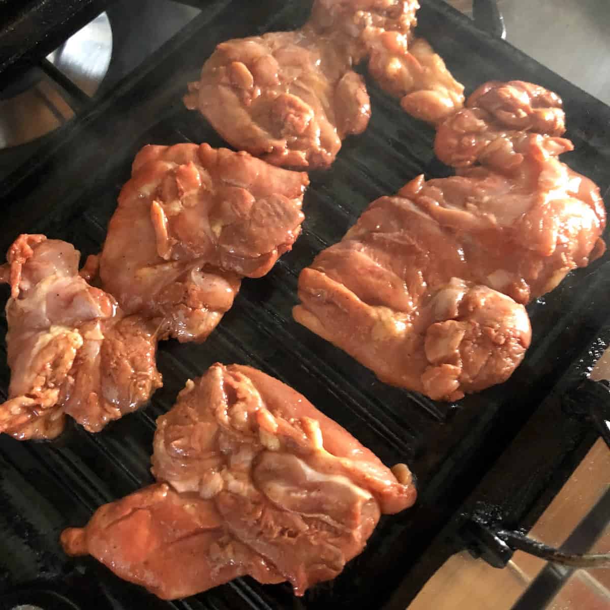 Pollo asado marinated chicken thighs added to a searing hot grill pan to cook, pollo asado al carbon on the stovetop.
