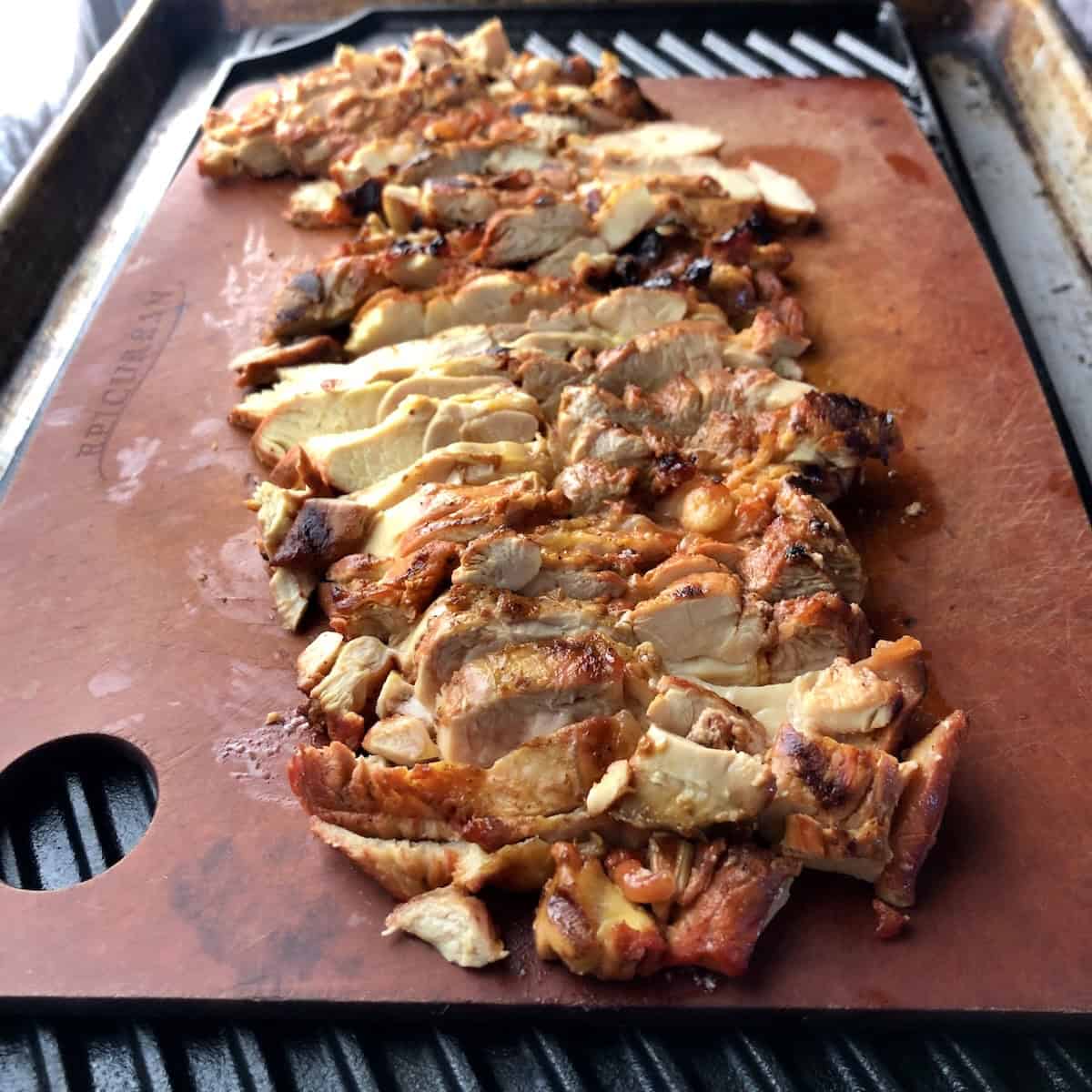 Grilled sliced pollo asado on an Epicurean cutting board on a Lodge cast iron grill pan looking juicy and tender, pollo al carbon ready to use or store.