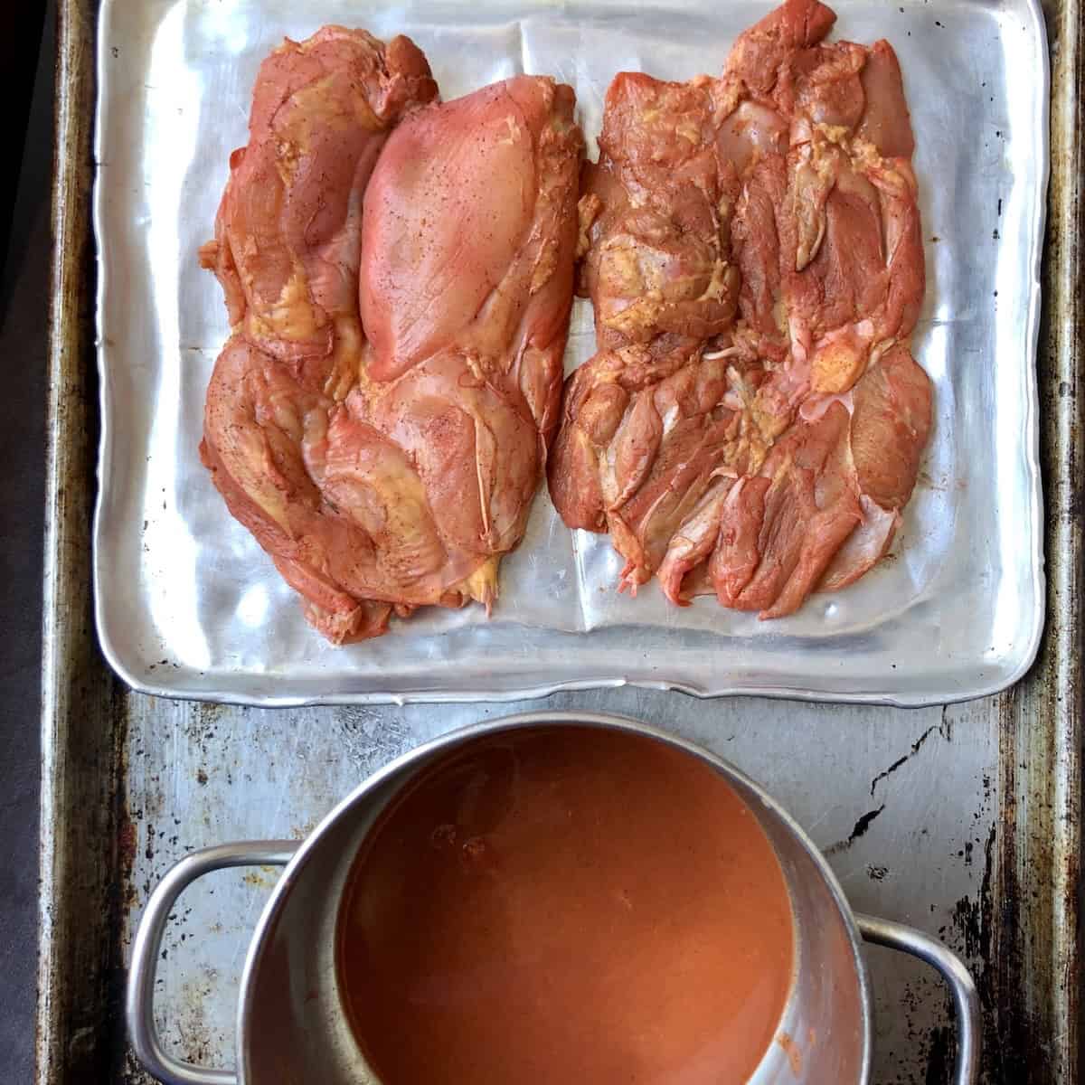 Marinated chicken thighs removed from the pollo asado marinade and completely patted dry and now a red-orange color, ready to brush with oil and grill, oven bake, or cook on the stovetop, next to the leftover marinade that can be cooked and used safely.
