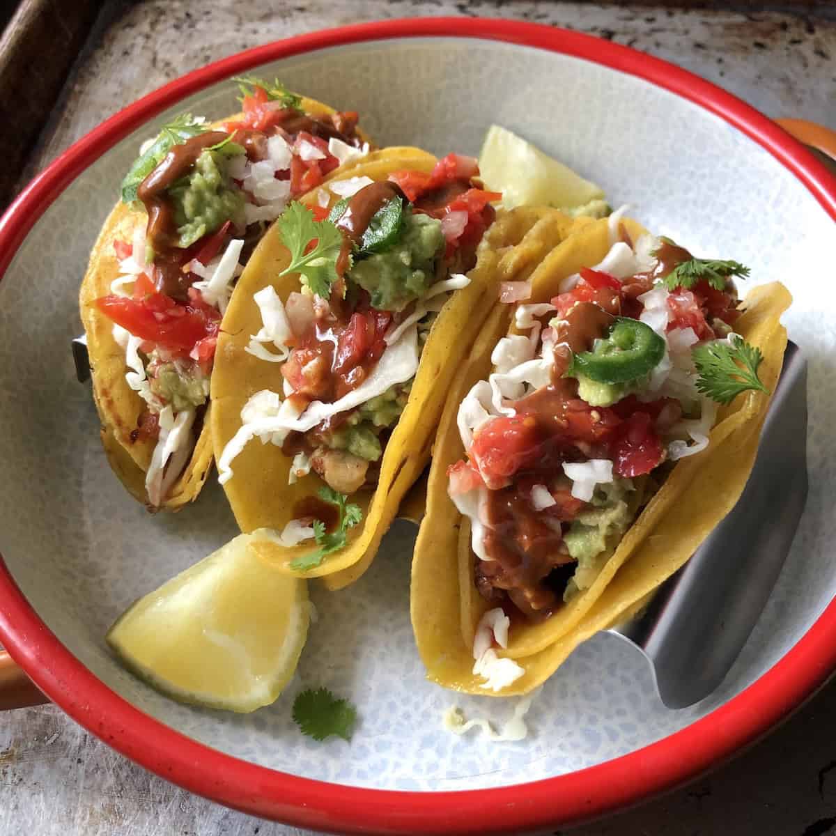 Three fully loaded pollo asado chicken tacos with Valentina hot sauce drizzled across the tops, mexican grilled chicken tacos ready to eat.

